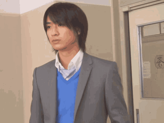 a man in a suit and blue sweater is standing in front of a door with chinese writing on it