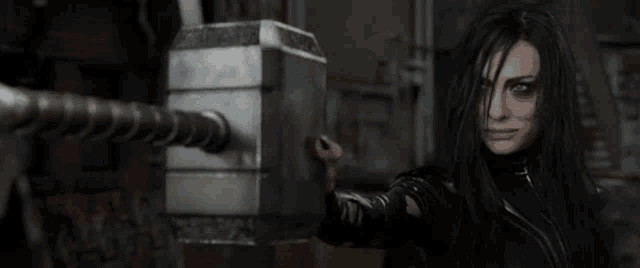 a woman with long black hair is holding a giant hammer in her hand .