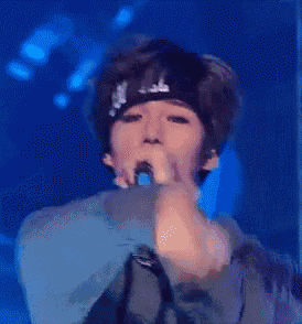 a young man wearing a bandana is singing into a microphone .