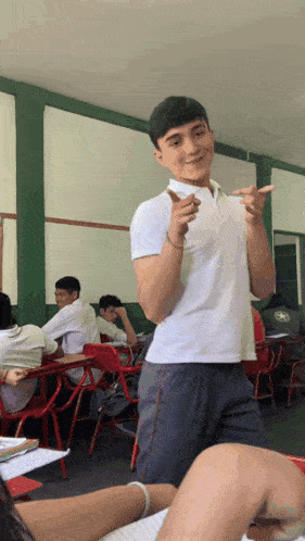 a young man in a white shirt is giving a thumbs up in a classroom