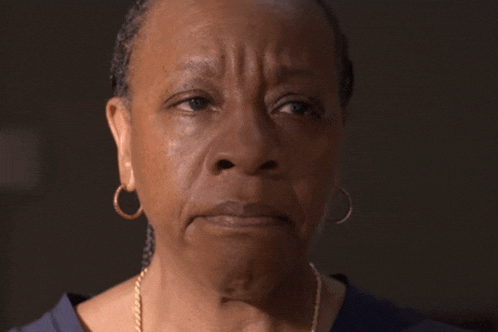a woman wearing hoop earrings and a necklace looks at the camera
