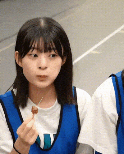 a girl wearing a blue vest with the letter w on it is eating something