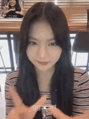 a girl with long black hair is making a peace sign with her hands while sitting at a table .