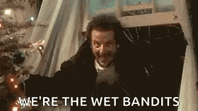 a man is standing in front of a christmas tree with the words `` we 're the wet bandits '' written above him .