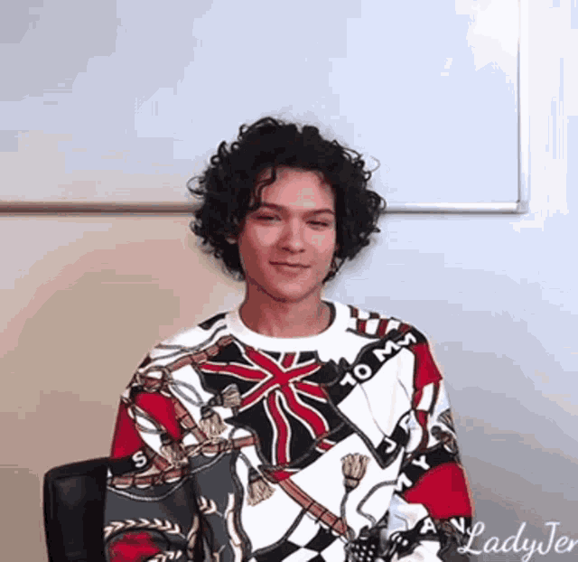 a man with curly hair wearing a sweater that says 10 mm on it
