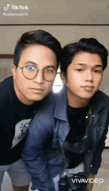 two young men are posing for a picture together . one of the men is wearing glasses .