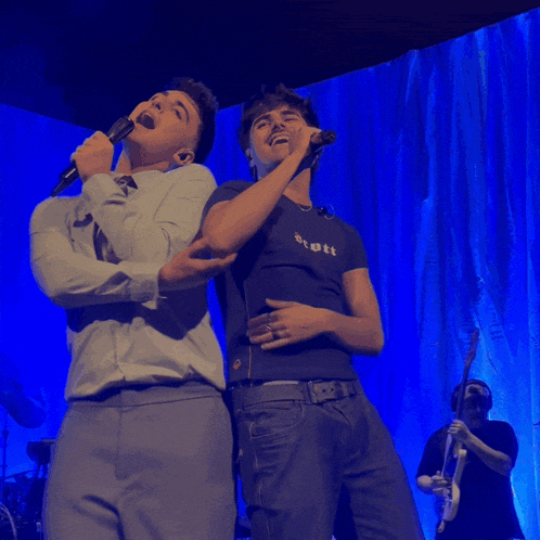 two young men singing into microphones on a stage