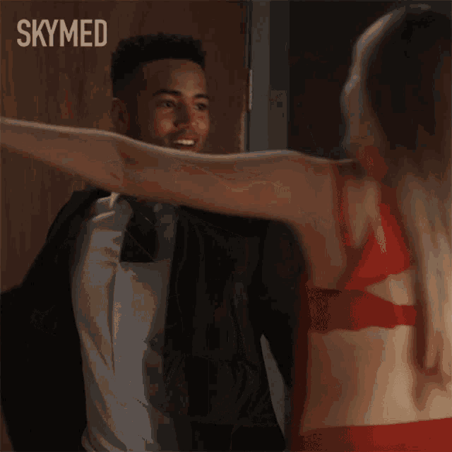 a man in a suit and tie is hugging a woman in a red bra in front of a skymed sign