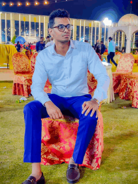 a man in a white shirt and blue pants sits on a red chair