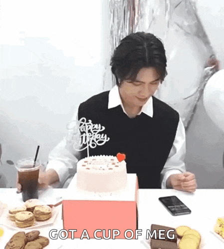 a man is sitting at a table with a cake and a cup of coffee and says `` got a cup of meg '' .
