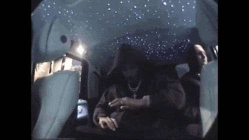 a man in a hoodie is sitting in the back seat of a car with a starry ceiling .