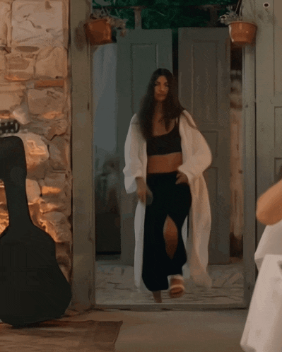 a woman in a crop top and black pants is walking through a doorway