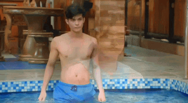 a shirtless man in blue shorts stands in a pool