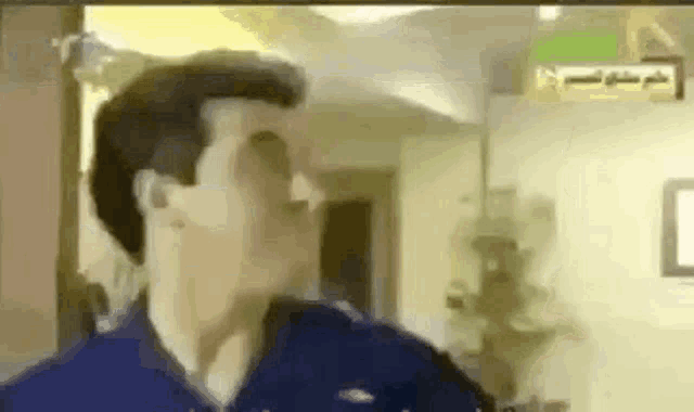 a man in a blue shirt is standing in a room with his mouth open .