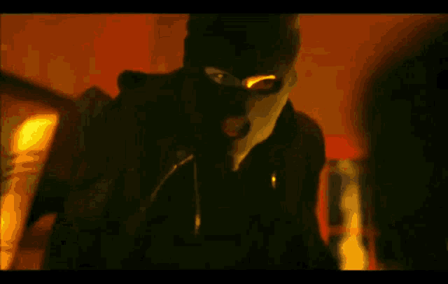 a man in a ski mask is holding a bottle in his hand in a dark room .