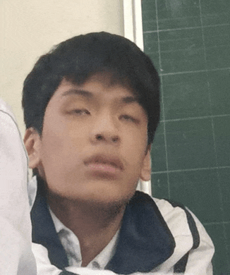 a young man sitting in front of a green chalkboard making a funny face