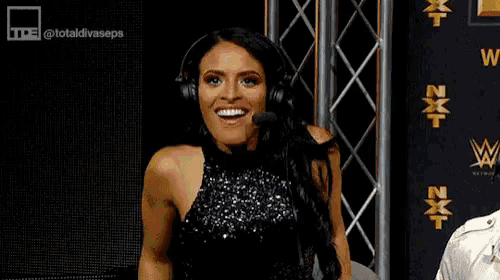 a woman wearing headphones and a black dress is smiling while sitting in front of a microphone .
