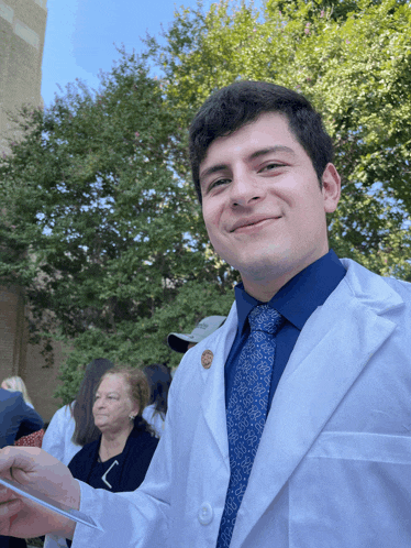 a man wearing a white coat and a blue tie is smiling for the camera