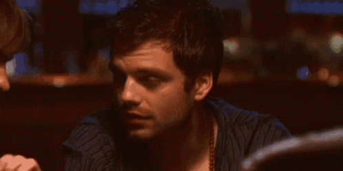 a man in a blue shirt is sitting at a table in a dark room .