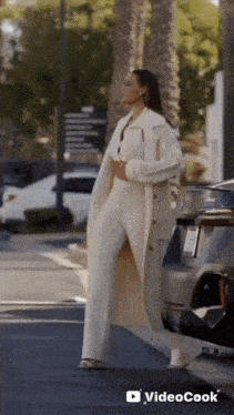 a woman in a white coat and white pants is walking down the street .