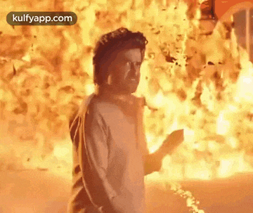 a man is standing in front of a large explosion .