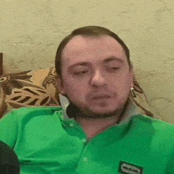 a man is sitting on a couch wearing a green shirt and making a funny face .