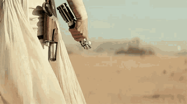 a person in a white dress is holding a light saber in the desert .
