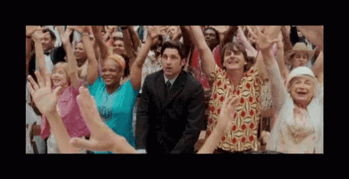 a large group of people are standing in a crowd raising their hands in the air .