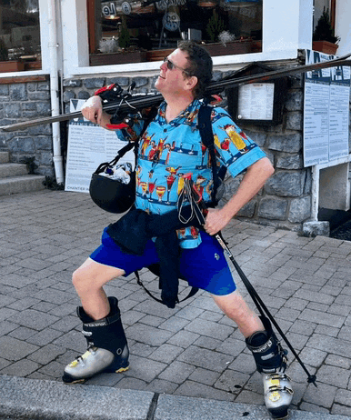 a man wearing ski boots and a shirt with a drink on it is holding a pair of skis