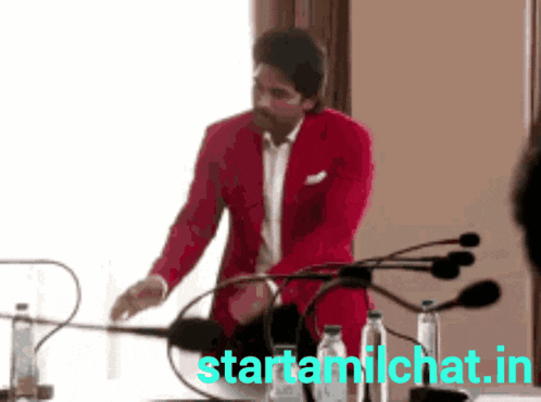 a man in a red suit is standing in front of a microphone with the website starttamilchat.in visible in the corner