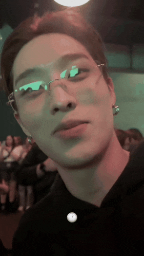 a man wearing glasses and earrings looks at the camera in a dark room
