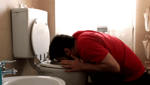 a man in a red shirt is vomiting in a toilet