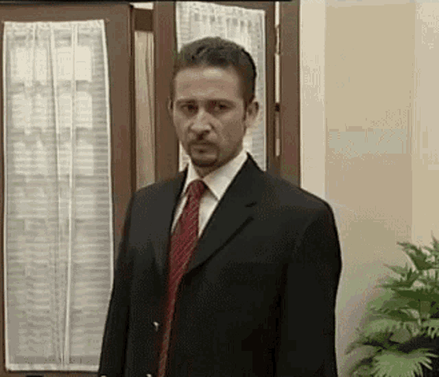 a man in a black suit and red tie is standing in front of a door
