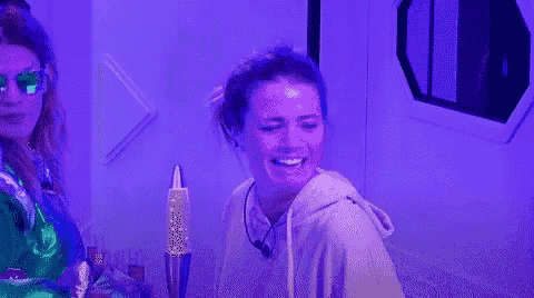 a woman is laughing in front of a purple wall while another woman looks on .