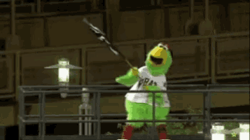 a green chicken mascot is standing on a balcony holding a flag