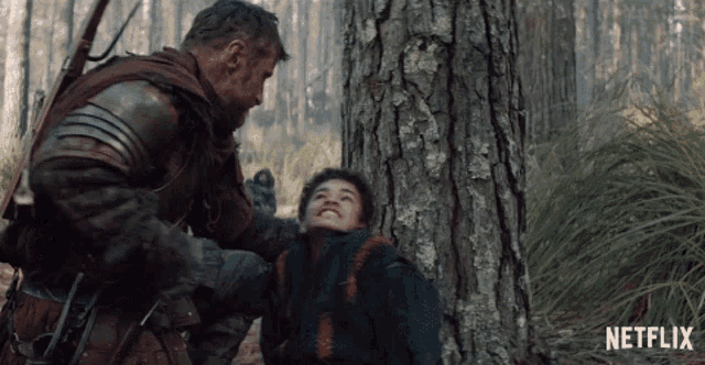 a man in armor is holding a young boy in a forest with a netflix logo in the corner