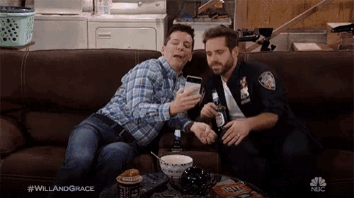 two men are sitting on a couch looking at a cell phone