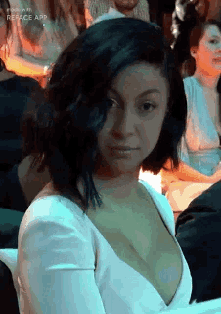 a woman in a white dress with a plunging neckline is sitting at a table in a crowded room .