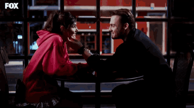 a man and a woman are looking at each other in front of a window with fox written on it