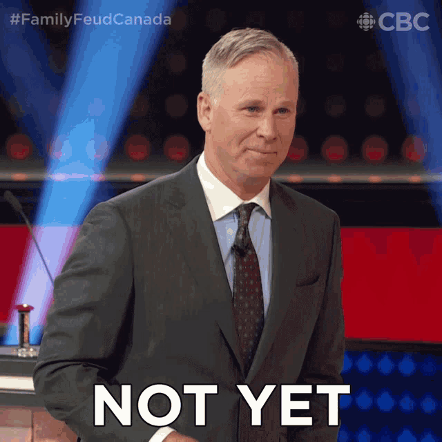 a man in a suit and tie says " not yet " in front of a microphone