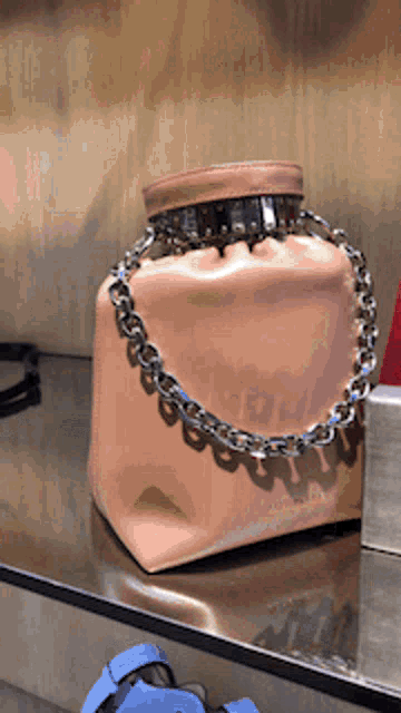 a pink purse with a chain around the handle sits on a shelf