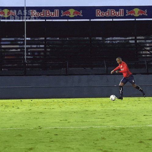 a man in a red shirt kicking a soccer ball in front of a red bull banner