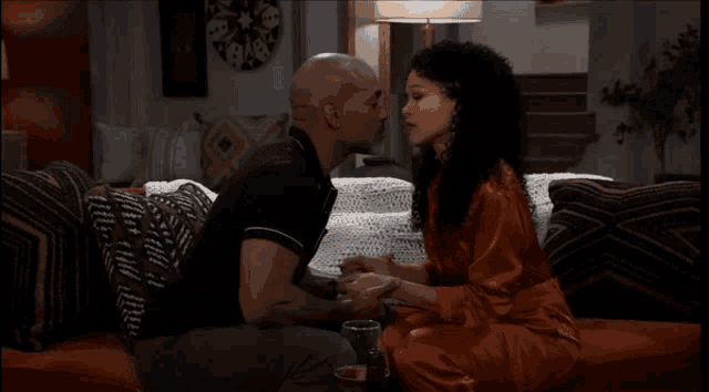 a man and woman kissing on a couch with a lamp in the background