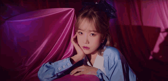 a girl in a blue jacket is laying on a pink couch with her hand on her face