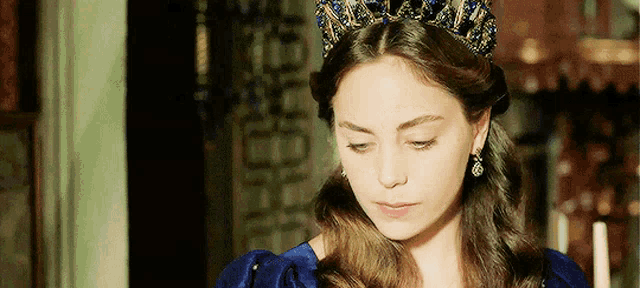 a woman wearing a blue dress and a crown is looking down