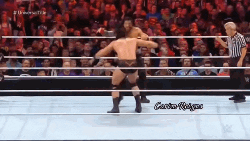 two men are wrestling in a wrestling ring with a referee standing behind them .