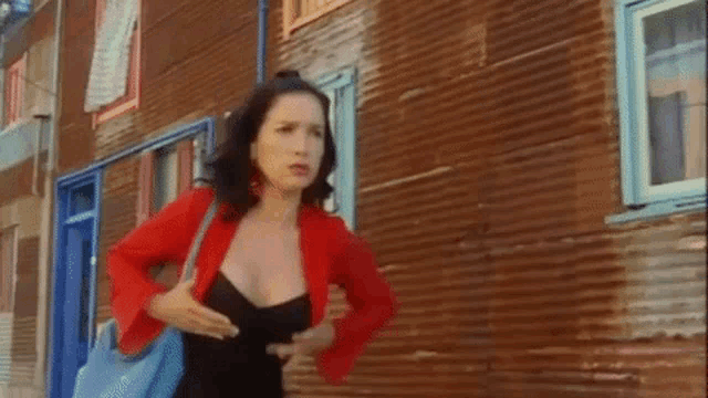 a woman in a black dress and a red jacket is standing in front of a building .