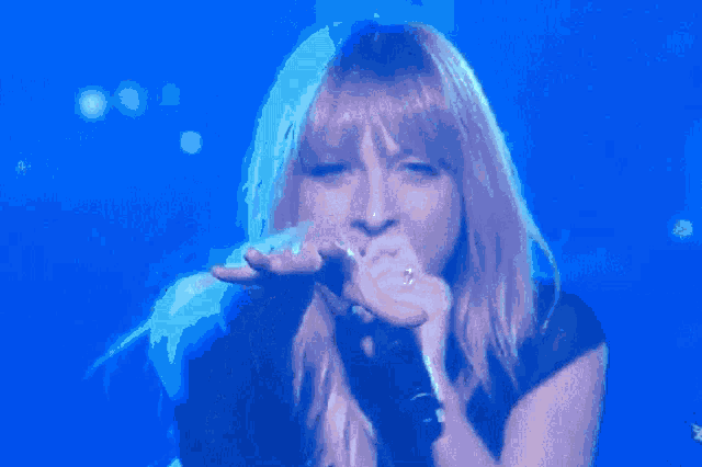 a close up of a woman singing into a microphone with a blue background