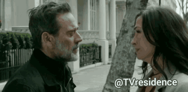 a man and a woman are standing next to each other on a sidewalk and looking at each other .