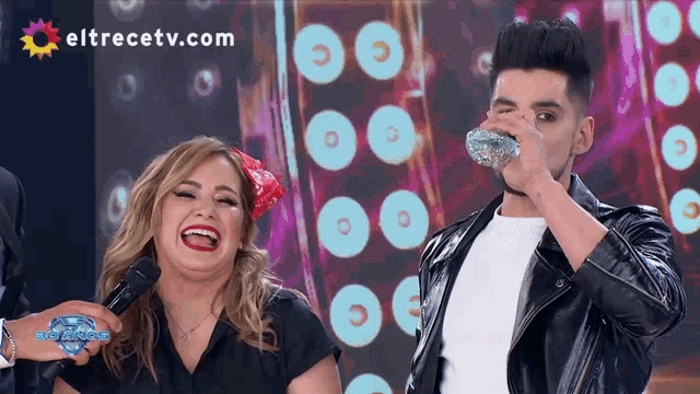 a woman laughs next to a man holding a microphone with eltrecetv.com on the bottom